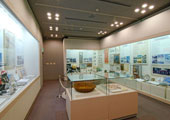 ダウンライト照明の部屋には、壁側三面の大きなスペースに資料・お皿・絵画・掛け軸などが展示され、中央にも展示ケースが置かれている。