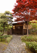 石畳の奥に純和風の引き戸の木月庵入口。右手前にある木は紅葉し赤く色づき、左の松の緑と対照的。